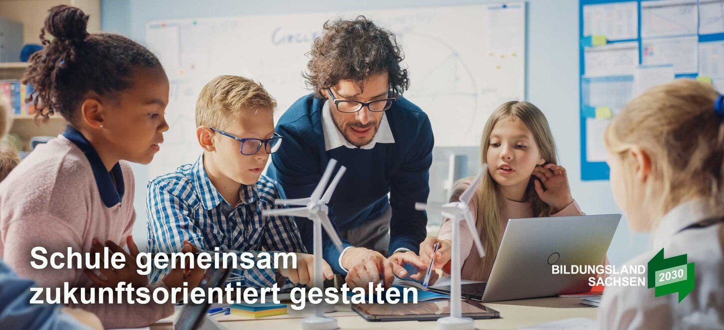 Das Foto zeigt eine Lehrkraft, welche vier Schülerinnen und Schülern an kleinen Windrädern etwas erklärt. Das Bild trägt den Schriftzug "Schule gemeinsam zukunftsorientiert gestalten".