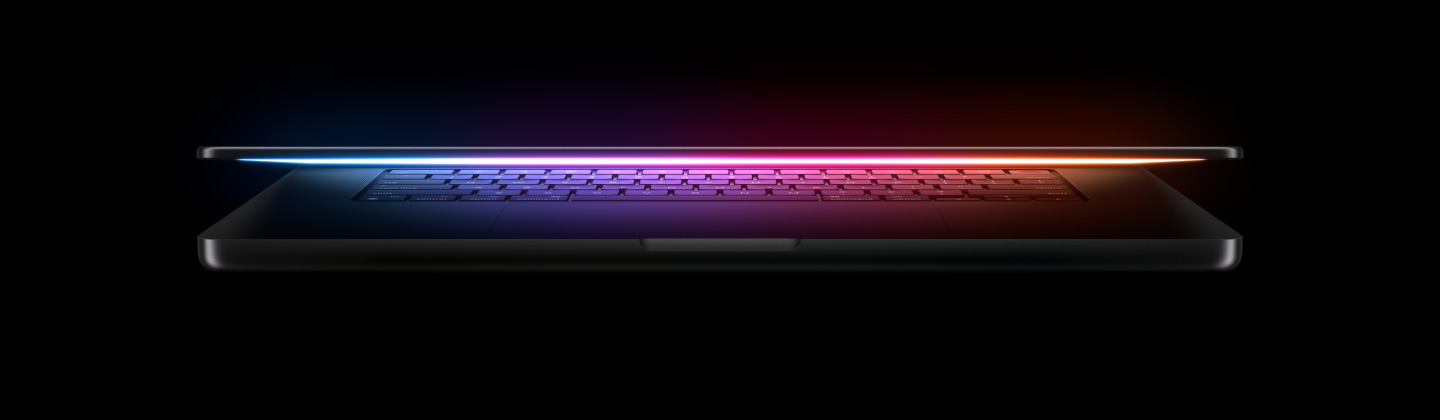 A slightly open MacBook Pro casts a multicoloured glow from the screen onto the keyboard