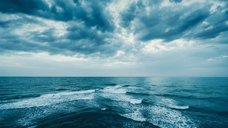 Waves across a dark blue sea with dark clouds fractures by light above