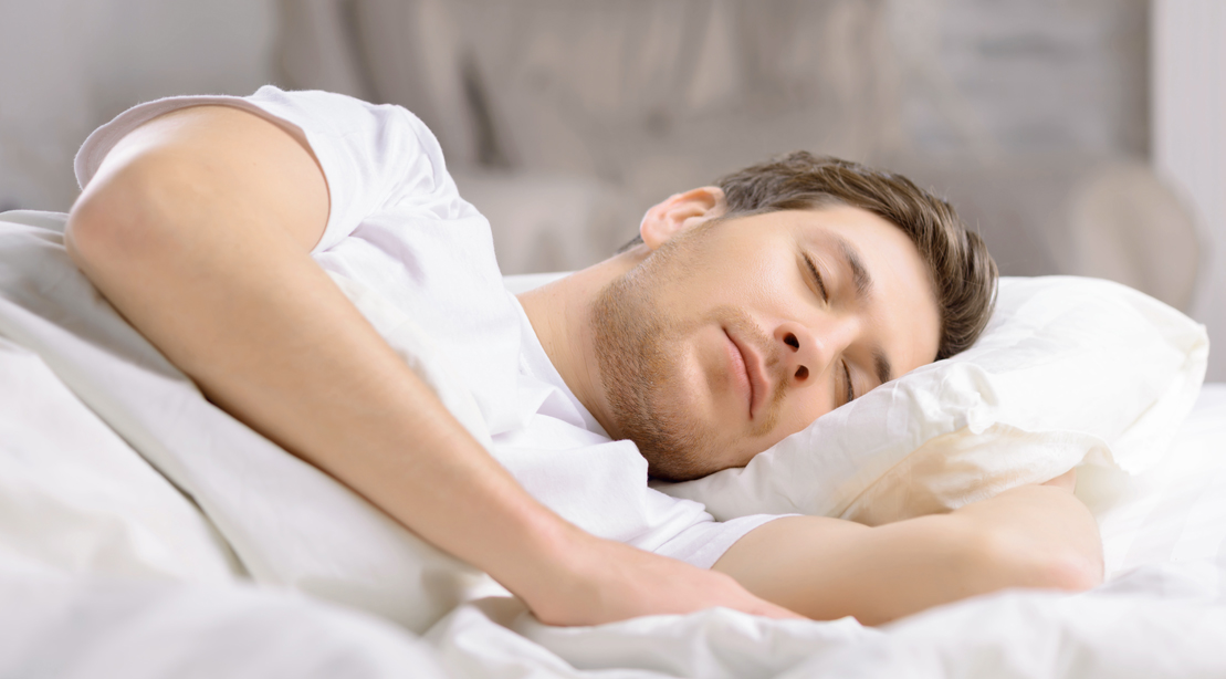 Man sleeping peacefully in a bed with white sheets for a sleep study