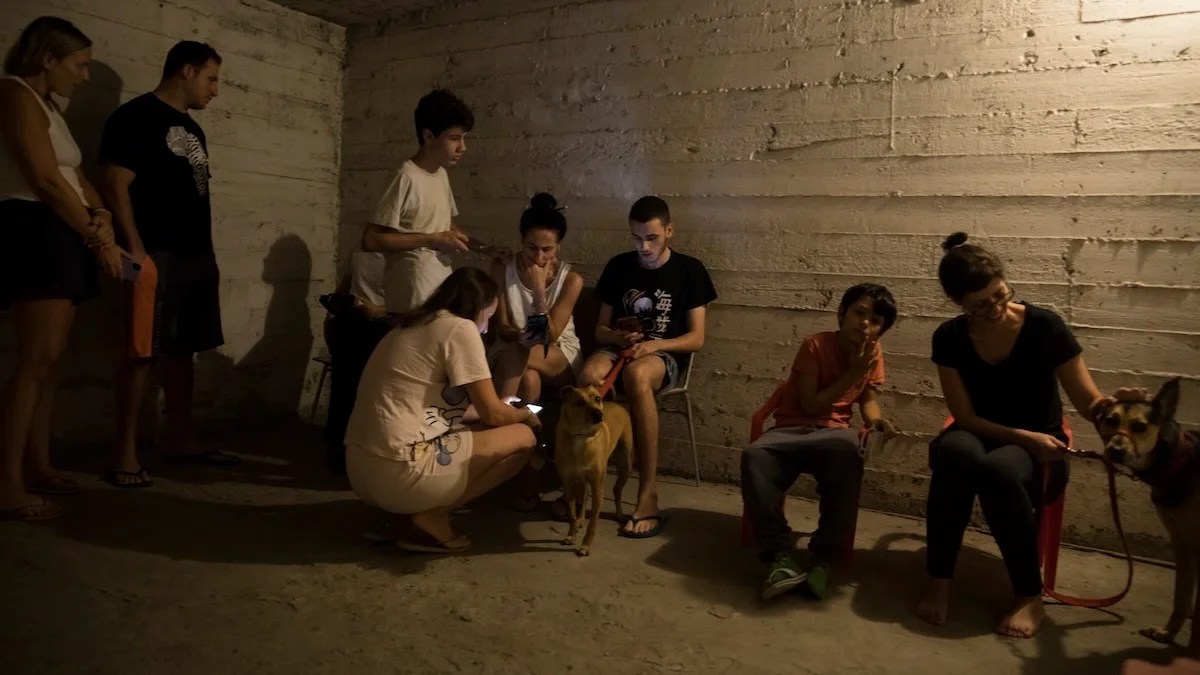 A group of people in a dim shelter, including women, children, and a dog.