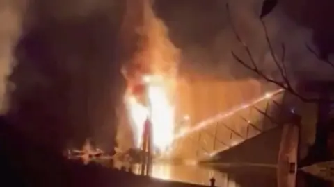 A burning bridge falls into a river at night