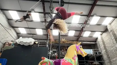 A woman doing acrobatics above a toy horse