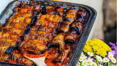 Auberginenröllchen mit Hackfleisch      Zutaten:  3 große Auberginen  Salz, Pfeffer aus der Mühle  120 ml Olivenöl extra vergine  1 TL edelsüßes Paprikapulver  1 TL getrockneter Oregano  1 TL gemahlener Kreuzkümmel  2 Zwiebeln  2 Knoblauchzehen  700 g Rinderhackfleisch  30 g Petersilie, fein gehackt  2 Prisen Zimt  500 G reife Tomaten  150 ml Rotwein      Zubereitung:  1. Den Backofen auf 190 Grad Umluft vorheizen.  2. Die Auberginen längs in etwa 1½ cm dicke Scheiben schneiden und in eine Schüssel geben. Mit Salz und Pfeffer bestreuen, dann 30 ml Olivenöl sowie je 1 Prise Paprikapulver, Oregano und Kreuzkümmel dazumischen.  3. Die Auberginen auf einem Blech verteilen und im vorgeheizten Backofen rund 25 Minuten backen.  4. Die Zwiebeln und den Knoblauch fein hacken. In einer Schlüssel das Hackfleisch mit Zwiebeln, Knoblauch, Petersilie, 40 ml Olivenöl, jeweils restlichem Kreuzkümmel, Paprikapulver und Oregano sowie Zimt, Salz und Pfeffer gut vermischen und etwa 5 Minuten kneten.  5. Jeweils 1 Esslöffel der Hackfleischfüllung auf die untere schmale Seite jeder gebackenen Auberginenscheibe geben und die Scheiben aufrollen. So lange fortfahren, bis alle Zutaten aufgebraucht sind.  6. Die Tomaten in Würfel schneiden und auf den Auberginen verteilen. Mit dem restlichen Olivenöl und dem Rotwein begießen. Im Backofen bei 185 Grad  7. Umluft etwa 30 Minuten backen.