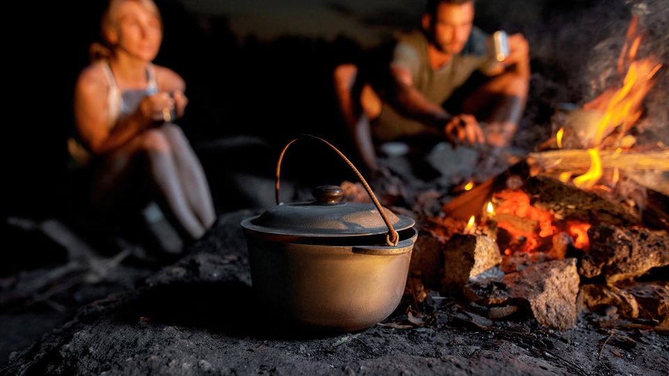 Eine Frau lässt einen Mann Essen probieren, im Vordergrund steht ein Dutch Oven.