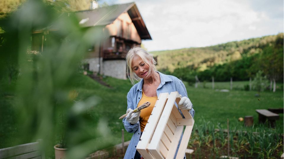 Eine ältere Frau streicht eine Holzkiste