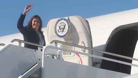 Kamala Harris steigt in ein Flugzeug und winkt lächelnd