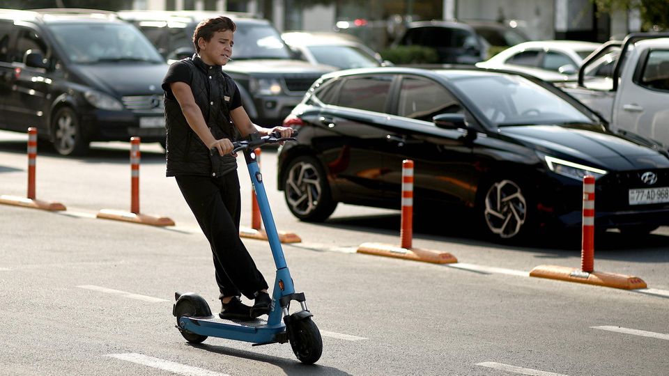 Ein Junge brettert mit einem E-Scooter an einer dicht befahrenen Straße vorbei