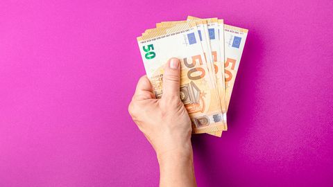 Eine Hand hält mehrere 50-Euro-Geldscheine vor pinkem Hintergrund