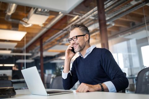 Vodafone Business: Geschäftsmann sitzt vor einem aufgeklappten Laptop und telefoniert mit dem Handy.