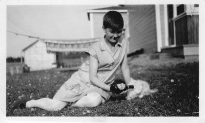 Young Girl Sitting on Lawn Feeding a Cat