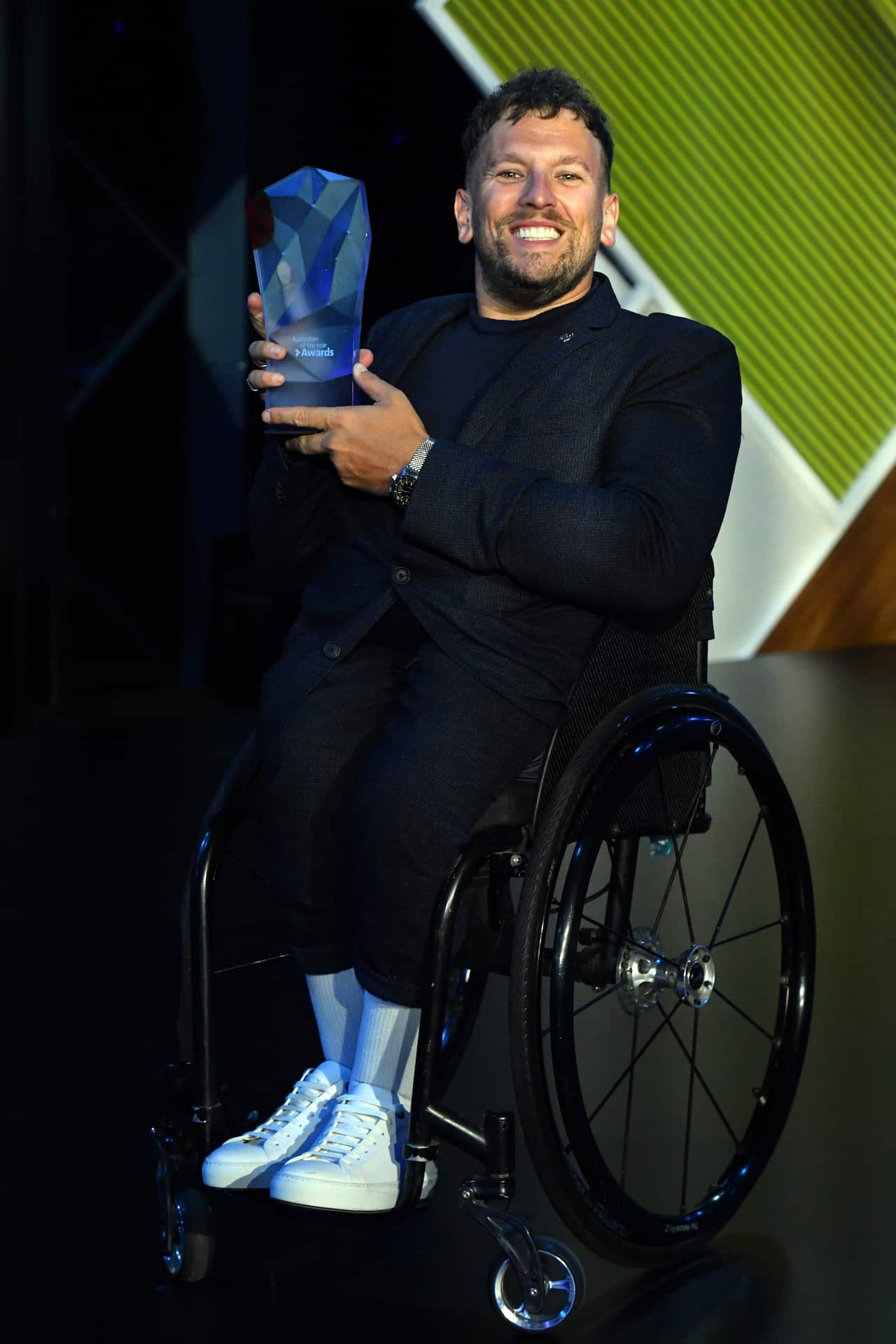 A man in a wheelchair smiles as he holds up a trophy