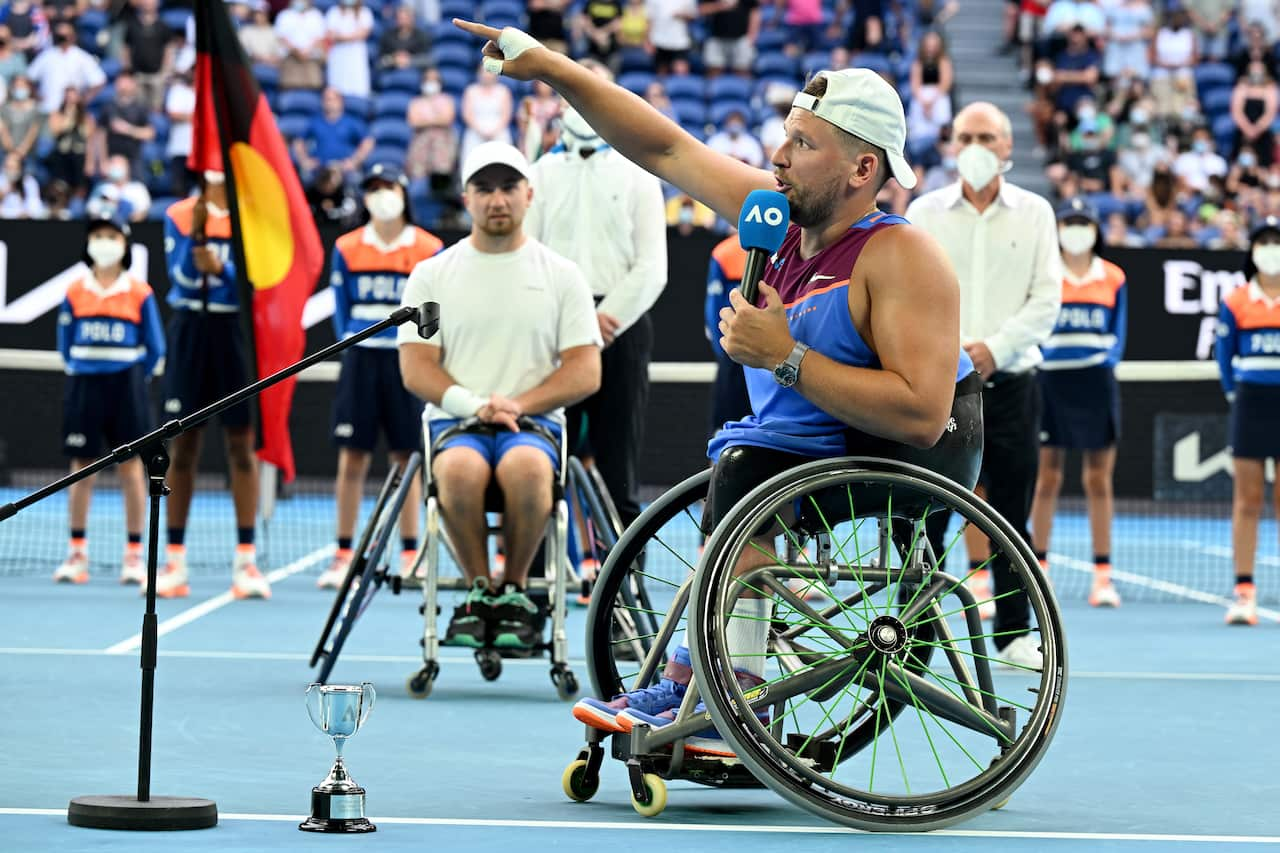 A man in a wheelchair speaks into a microphone on a tennis court