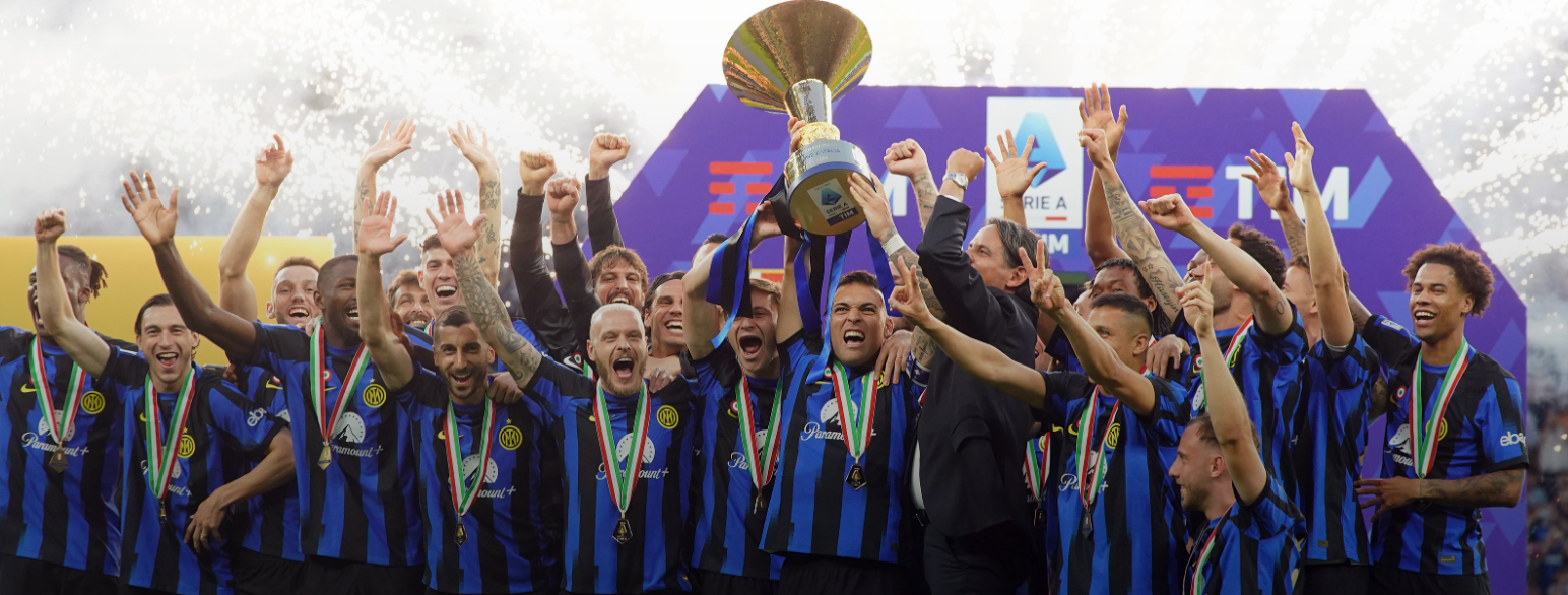 fotballspillere står på banen etter kampen med en pokal og hever armene i været og feirer.