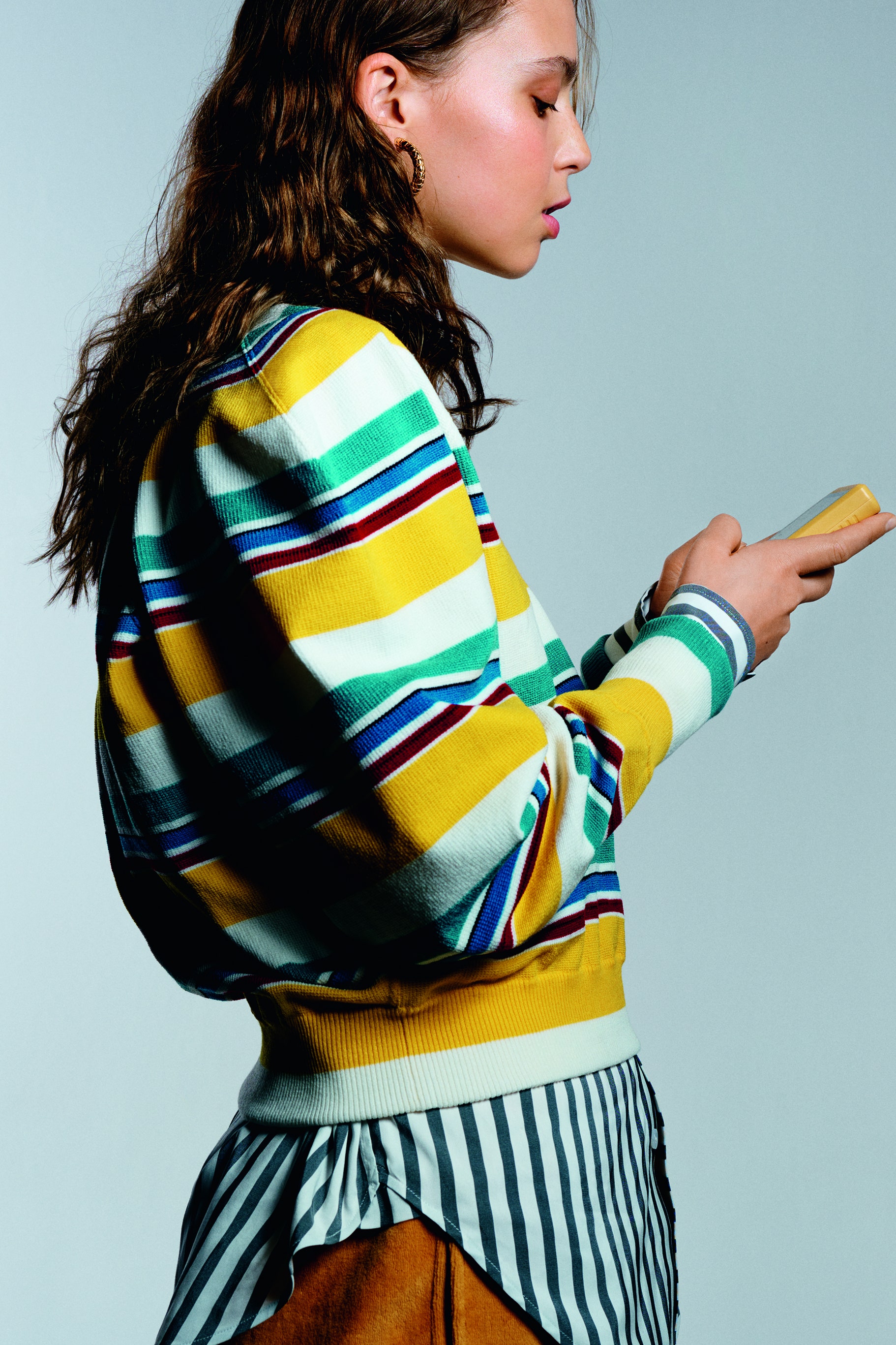 Side view of model wearing knitted woolen sweater striped shirt trousers and earrings