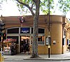 An orange building with an illuminated, blue sign reading "HOLLAND PARK STATION" in white letters and people walking in front all under a white sky