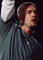 Justin Timberlake, performing at a concert, raising his right arm.