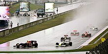 Photo de plusieurs monoplaces de Formule 1 roulant sous la pluie, à l'approche d'un virage