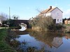 Bridge over still water with a house to the right.