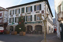 Photographie d’un édifice aux volets verts, avec quatre arches, un sapin dressé devant la façade.