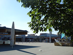 Heutiges Bahnhofsgebäude von Süden her gesehen mit allen Veränderungen und Anbauten, der Bahnhofsplatz vorne und der Bushof „Bahnhof Süd“ links