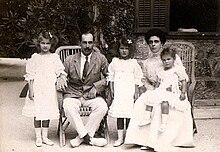 Photographie en noir et blanc montrant une famille composée d'un homme, d'une femme et de trois petites filles posant assis en extérieur.