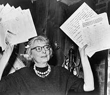 Woman in glasses waving documents in air.