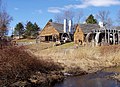 A complex of wooden barn-like buildings stands on a hillside. Water wheels for providing mechanical power are visible on the outsides.