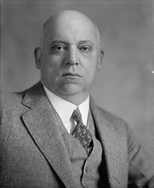 A black and white image of a bald man in his fifties wearing a suit