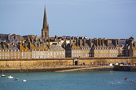 Vue de la ville depuis la mer, avec d'imposantes murailles au premier plan, et des maisons s'élevant derrière elles.