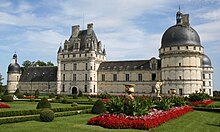 Photographie d'un imposant château à pierres blanches, présentant une tour centrale carrée et à toit droit, une aile droite terminée par une large tour ronde à toit en dôme, une aile gauche plus petite, terminée par une petite tour ronde. Au premier plan, un jardin à la française : herbe tondue, buis et parterre de fleurs.