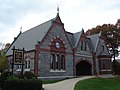 A building of stone and brick, with three steep gables and a slate roof. The central bay has an arched entrance. A sign to the left reads "Quincy Historical Society; Museum and Library".