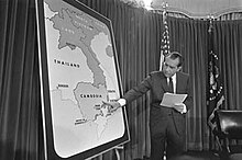 Nixon se tient devant une grande carte de l'Indochine et montre le Cambodge du doigt.