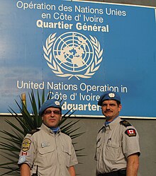 deux militaires de l'ONU portant des bérets bleus au quartier général de l'opération de l'ONU. en Côte d'Ivoire devant l'emblème de l'opération de l'ONU en Côte d'Ivoire