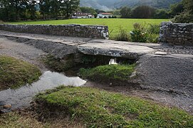 Vue d’un pont rustique formé d’une grande lauze sur un ruisseau.