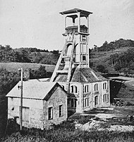 Bâtiment carré surmonté d'une tour en béton équipée de deux bigues de contrefort.