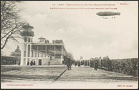 Photographie en noir et blanc d'un dirigeable survolant un hippodrome.