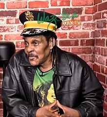 Majek Fashek sporting a Bob Marley t-shirt and wearing a military-style hat