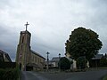 À droite, l'église, à gauche, la mairie, au centre, une croix monumentale de la crucifixion de Jésus