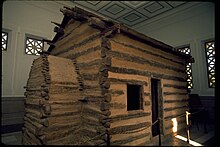 A log house on display inside a larger building.