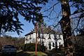 A large two story colonial frame house, five windows wide and three deep. It has a hip roof and two chimneys. The second floor windows have Christmas greenery below them, and the word Noel has been hung below the central window and above the front door.