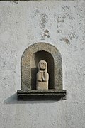 Photographie d'une niche de façade en granit, contenant une statuette.