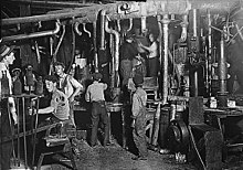 Une vieille photo en noir et blanc montre une douzaine d'enfants et d'adultes travaillant dans une usine.