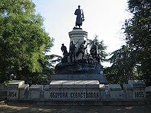 Frontale Farbfotografie eines Denkmals mit kyrillischem Titel und den Jahreszahlen 1854 und 1855 auf einer Steinmauer. Der untere Sockel hat einen gegossenen Felsen mit einigen Soldatenfiguren darauf, die einen weiteren Sockel mit einem General umkreisen. An beiden Seiten des Denkmals sind Bäume.