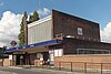 A red-bricked building with a rectangular, dark blue sign reading "WEST ACTON STATION" in white letters all under a blue sky with white clouds