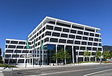 White company building at a crossroads, lined with trees on the left