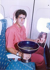 A man sitting in a blue seat, holding a trophy and a magazine