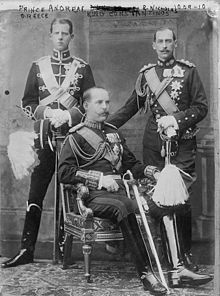 Cliché noir et blanc. 3 hommes en uniforme militaire. Au milieu, assis, de trois-quarts. 2 autres, de face, debout.