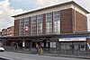 A brown-bricked building with a flat-slabbed roof and six columns of windows on the front face standing below a blue sky with white clouds