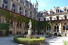 Photographie d'une cour. Au centre se trouve une statue entourée par des bâtiments anciens.